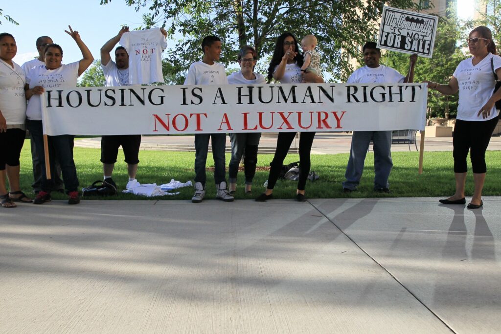 people in a line holding a banner that says housing is a human right, not a luxury
