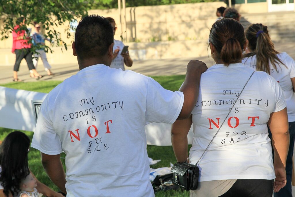 A couple with their back to the camera with shirts that say my community is not for sale